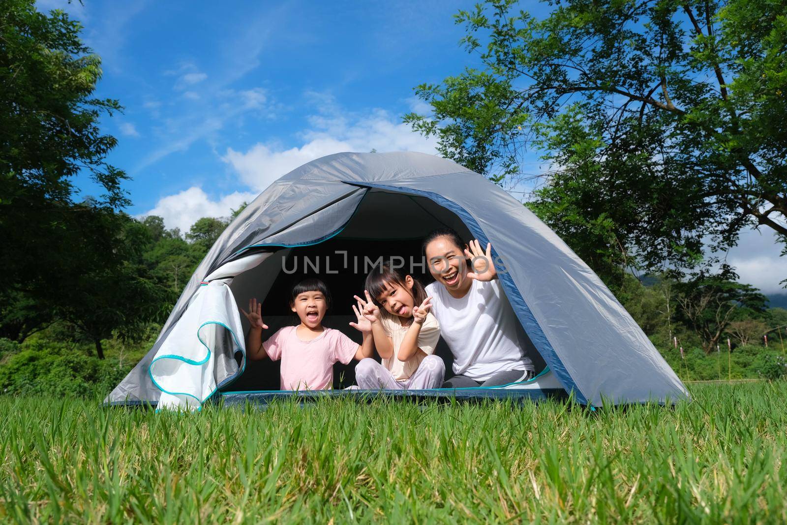 Happy family, mother and her daughters playing together in a camping tent at the campsite during a summer vacation in the countryside.
