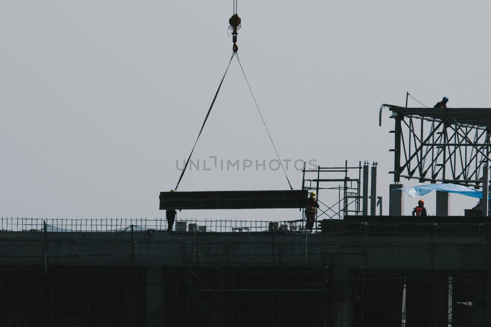 A large construction site with busy cranes. Tower cranes working on a construction site lifts a load at high-rise building in evening. by TEERASAK