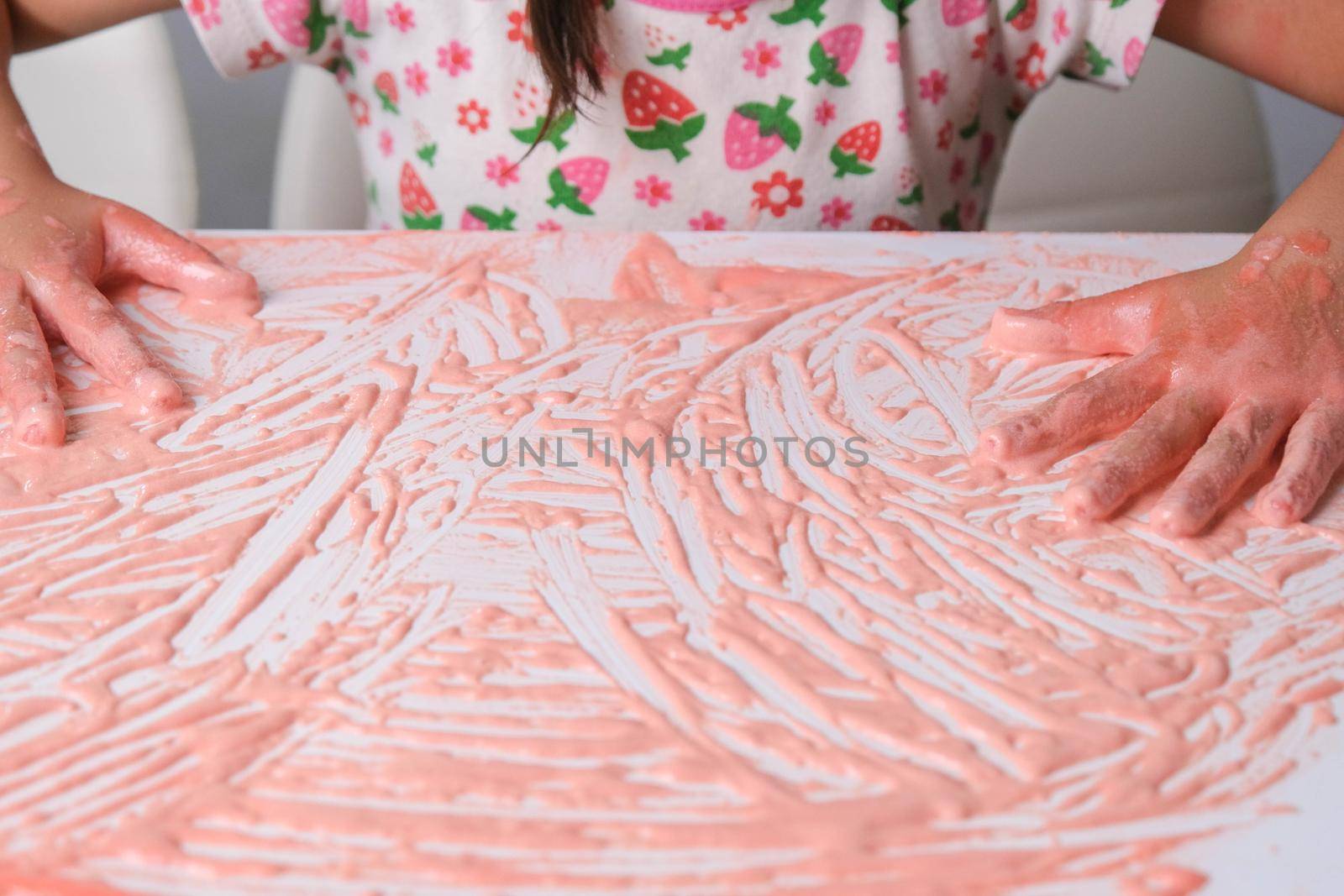 Little girl paints on a white table with colored salt, close up. Colored salt art. DIY Play and Learn Activities for Kids.