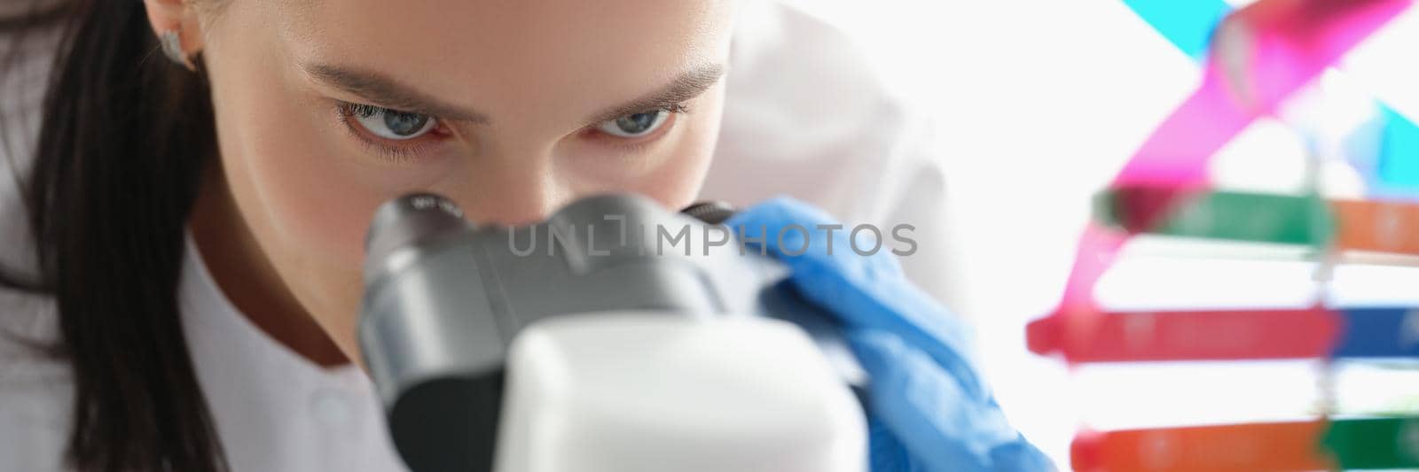 Woman scientist looking through a microscope, studying dna, face close-up. Hereditary information, decoding of the human genome