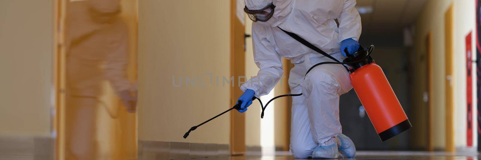 A man in a protective suit splashes from a cylinder onto the plinth in the corridor. Disinfection of premises, spread of viruses and harmful microorganisms