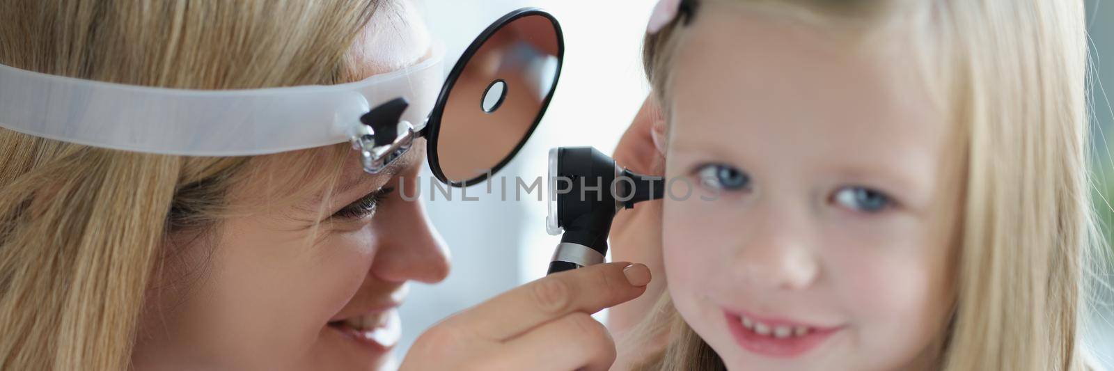 Otorhinolaryngologist examines the ear of a little girl, close-up. Woman doctor smiling, optimal treatment of ear inflammation