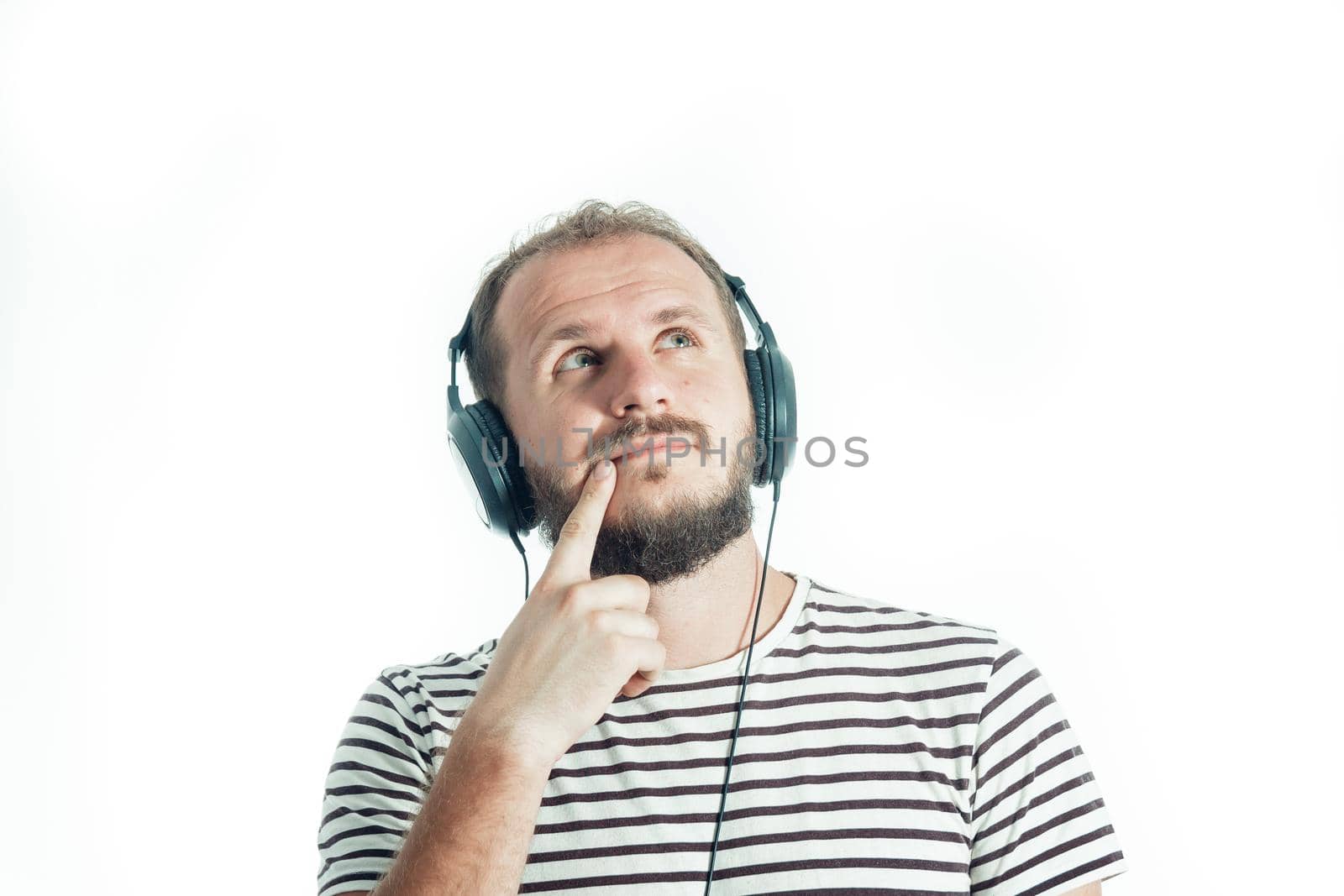 Meditative bearded happy man in a striped T-shirt listens to music with big headphones. 30-35 years old. Isolated by Rom4ek