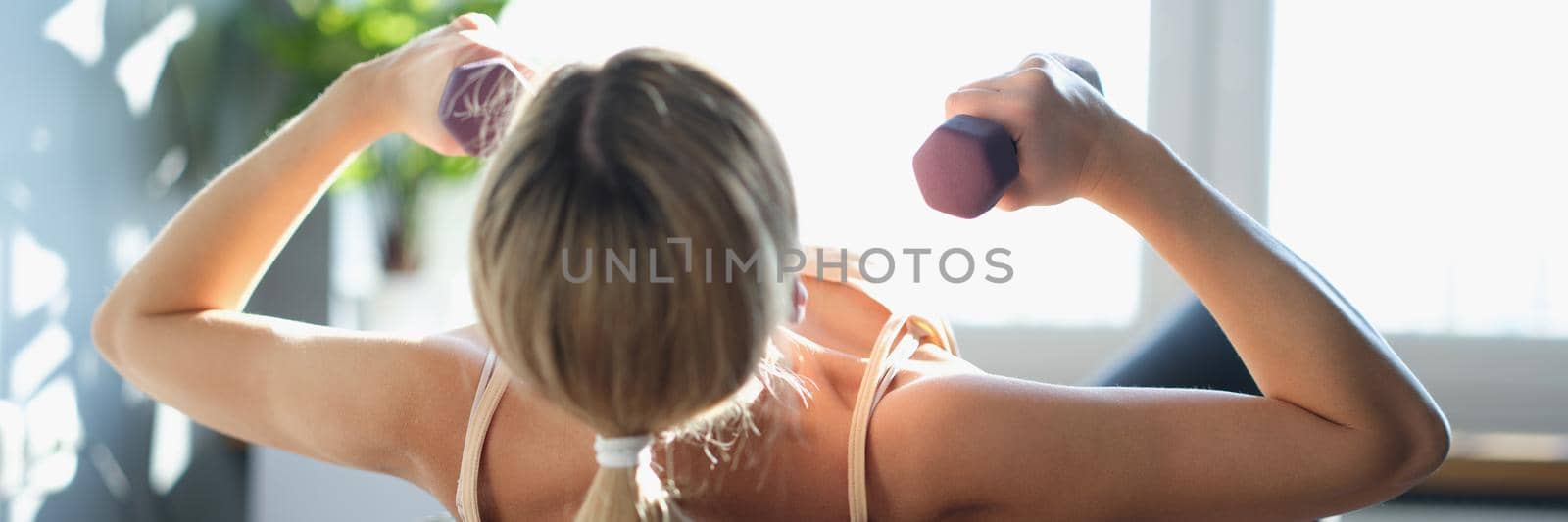 A woman lies on a sports ball with dumbbells in her hands by kuprevich