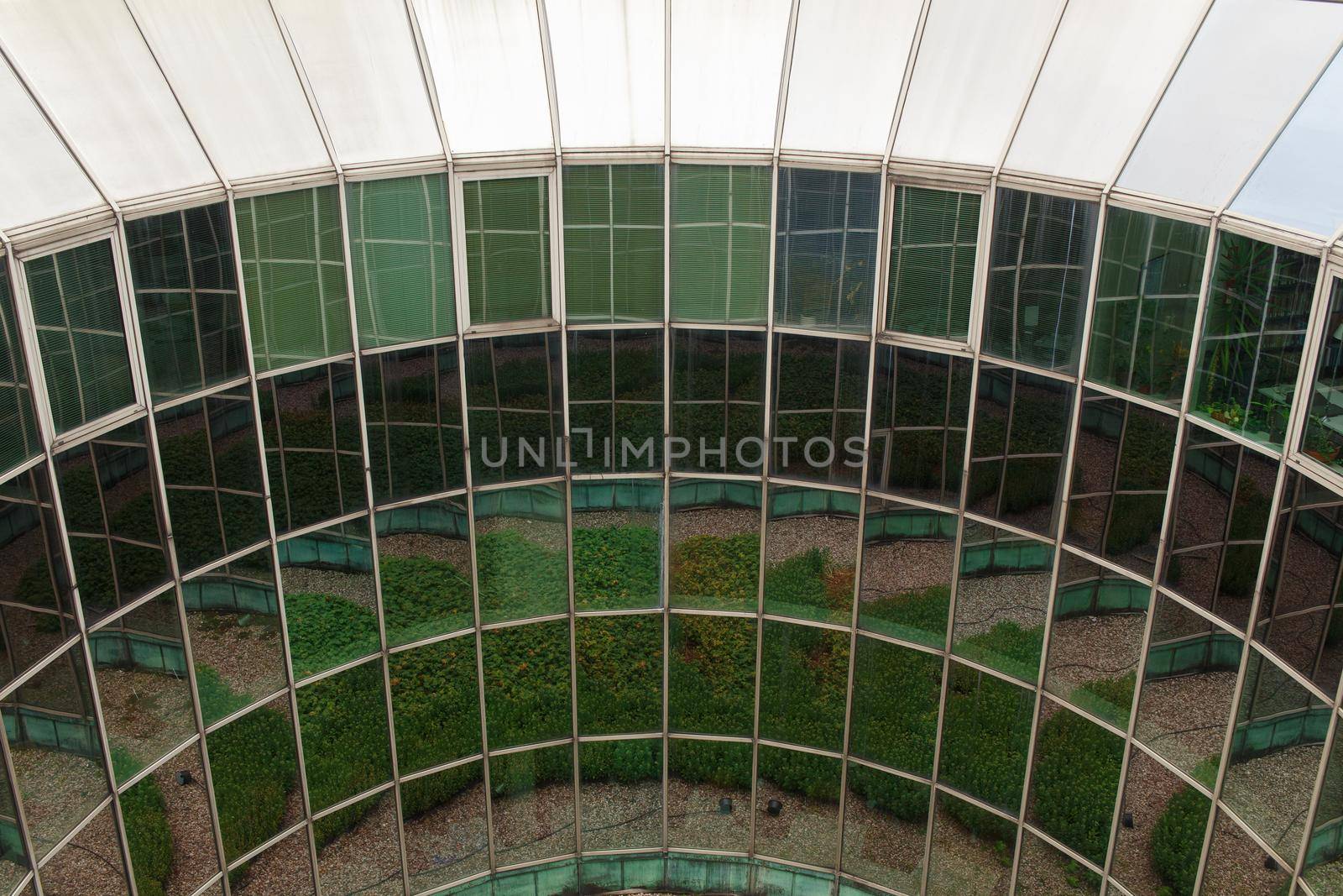 Fully glazed rounded wall of modern urban building. Numerous reflections of the courtyard with landscaping create a whimsical pattern.