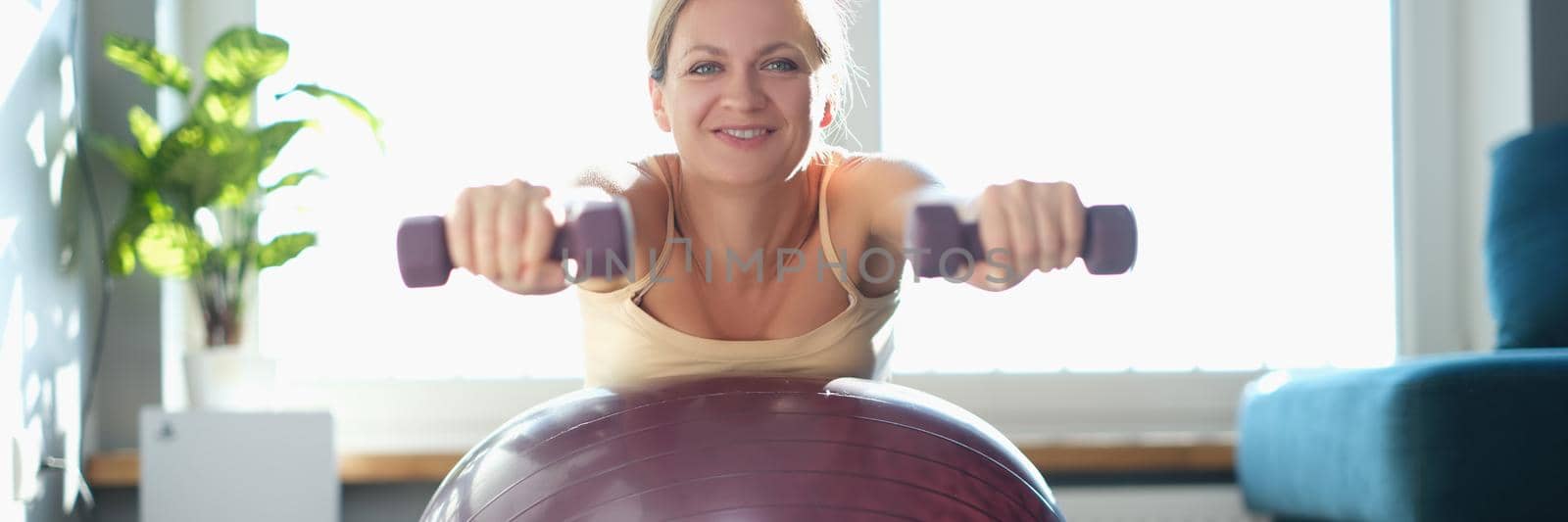 Woman doing exercises with dumbbells on a sports ball by kuprevich