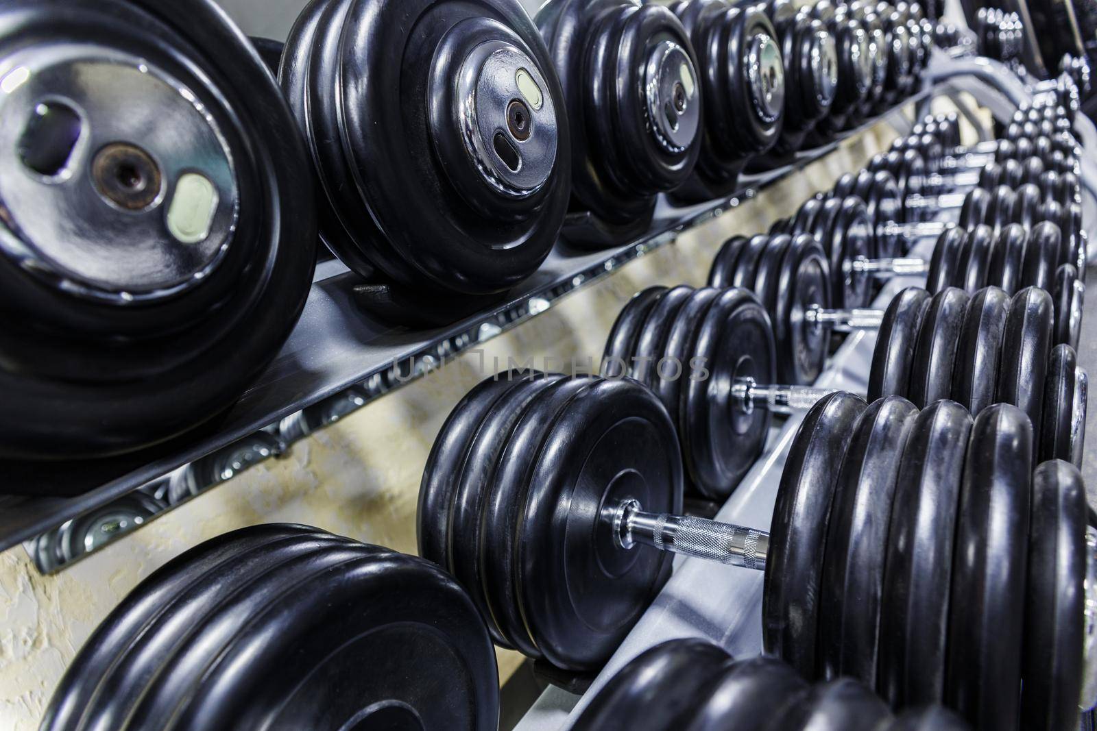 Black dumbbell set. Close up many rubberized dumbbells on rack in sport fitness center , Weight Training Equipment concept