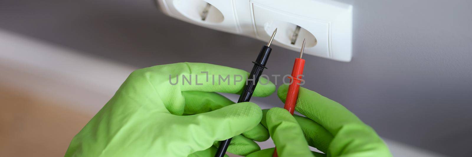 Measuring voltage with a multimeter, hands in rubber gloves close-up. Measuring instrument for electrical repair and maintenance