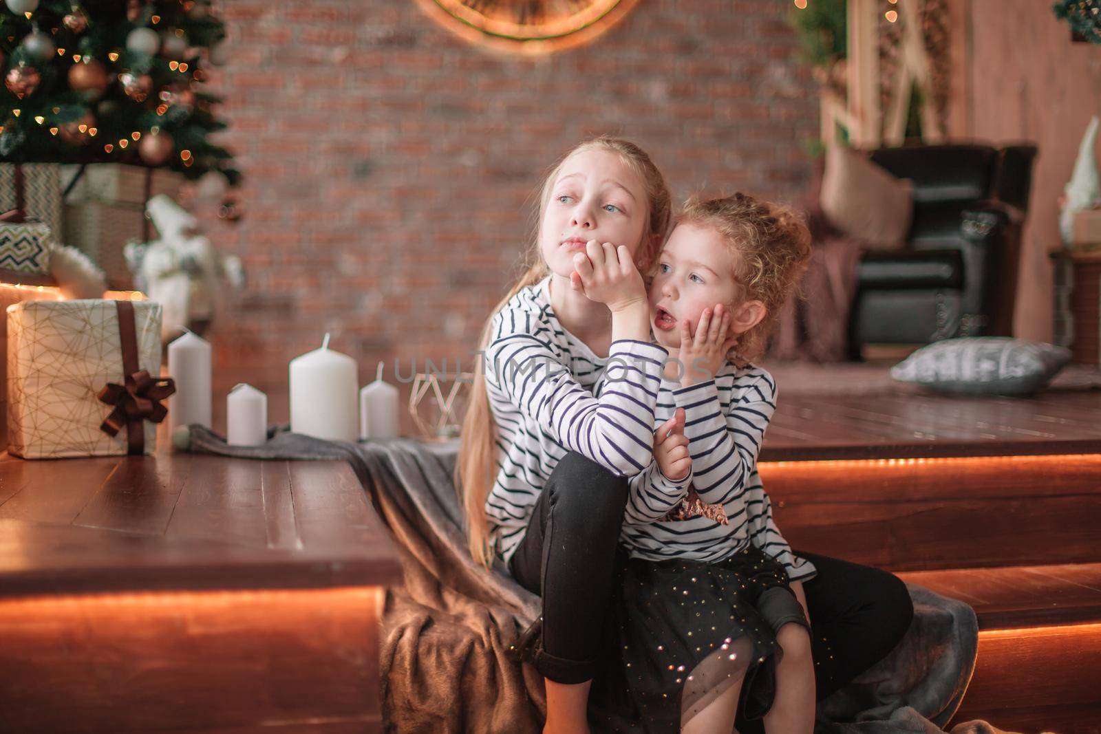 two little sisters talk sitting in a cozy living room . the concept of Christmas