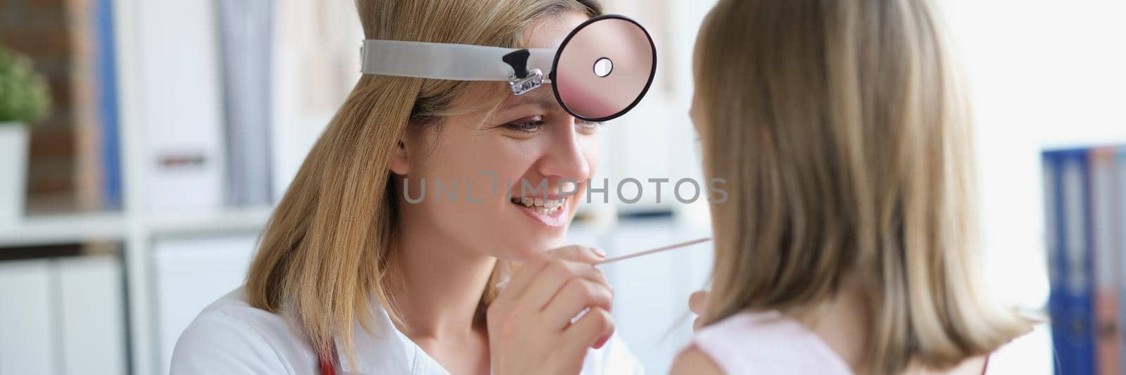 Children's otorhinolaryngologist examines the throat of a little girl. Woman doctor smiling, child health status