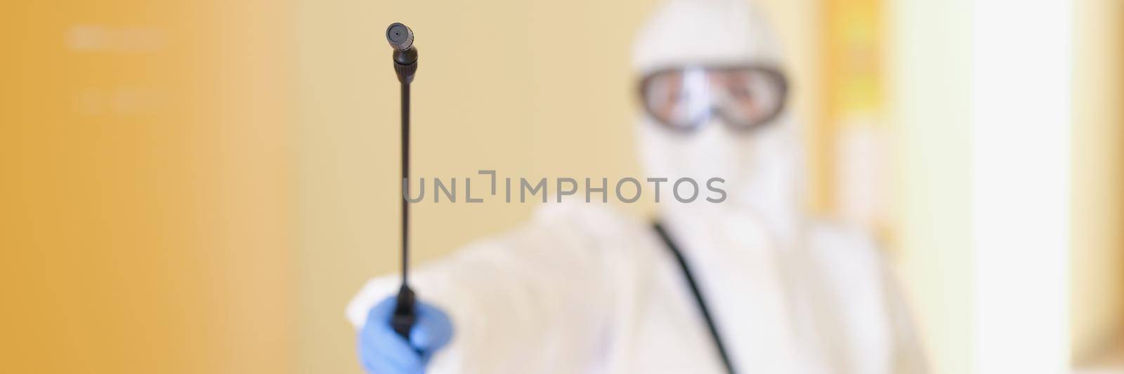 A man in a protective suit holds a sprayer, close-up, blurry. Equipment for high quality professional disinfection