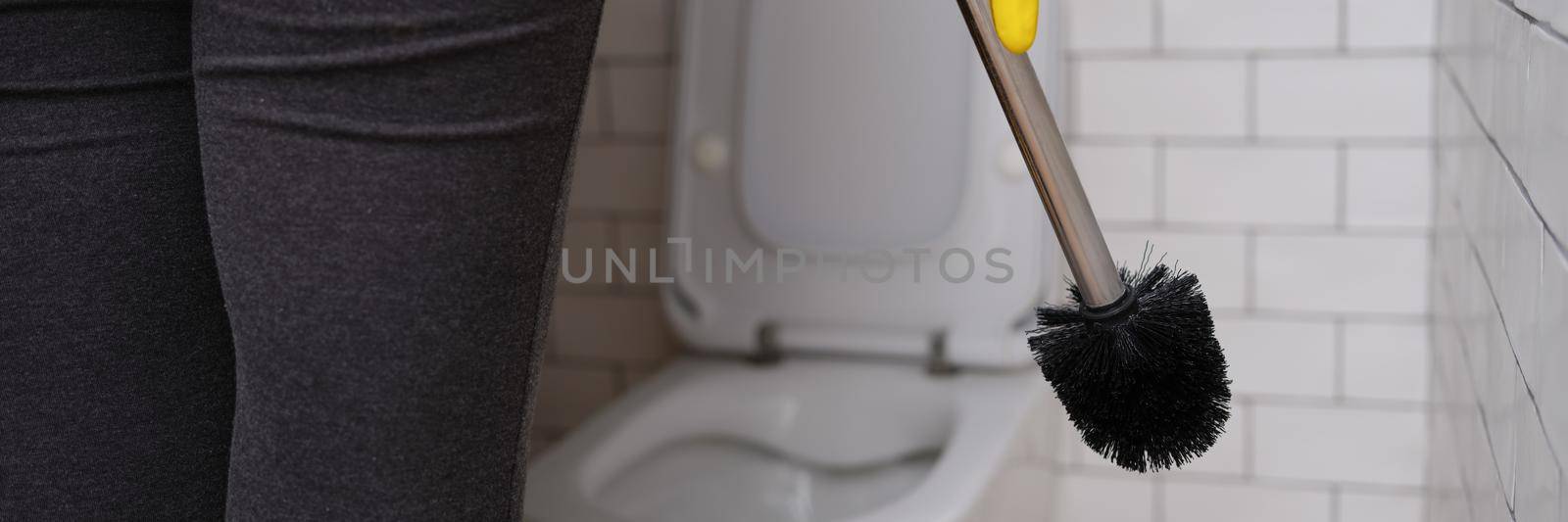 A woman in the toilet holds a brush for cleaning the toilet bowl, close-up. Disinfection and cleaning agent for plumbing in the wc