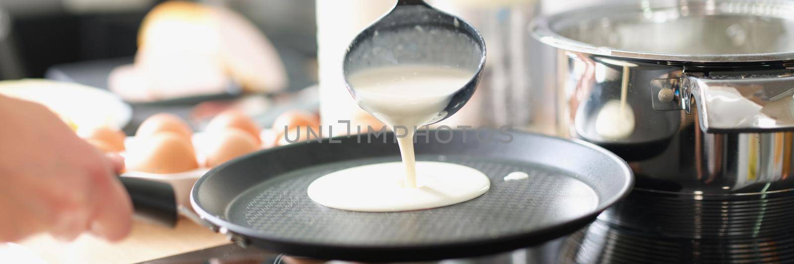 A man fries pancakes in a frying pan at home in the kitchen, close-up. Organic ingredients for batter preparation