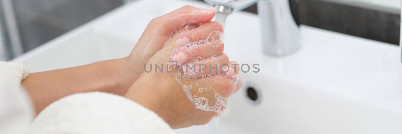 A woman in a dressing gown washes her hands with soap, close-up. Personal hygiene during a pandemic