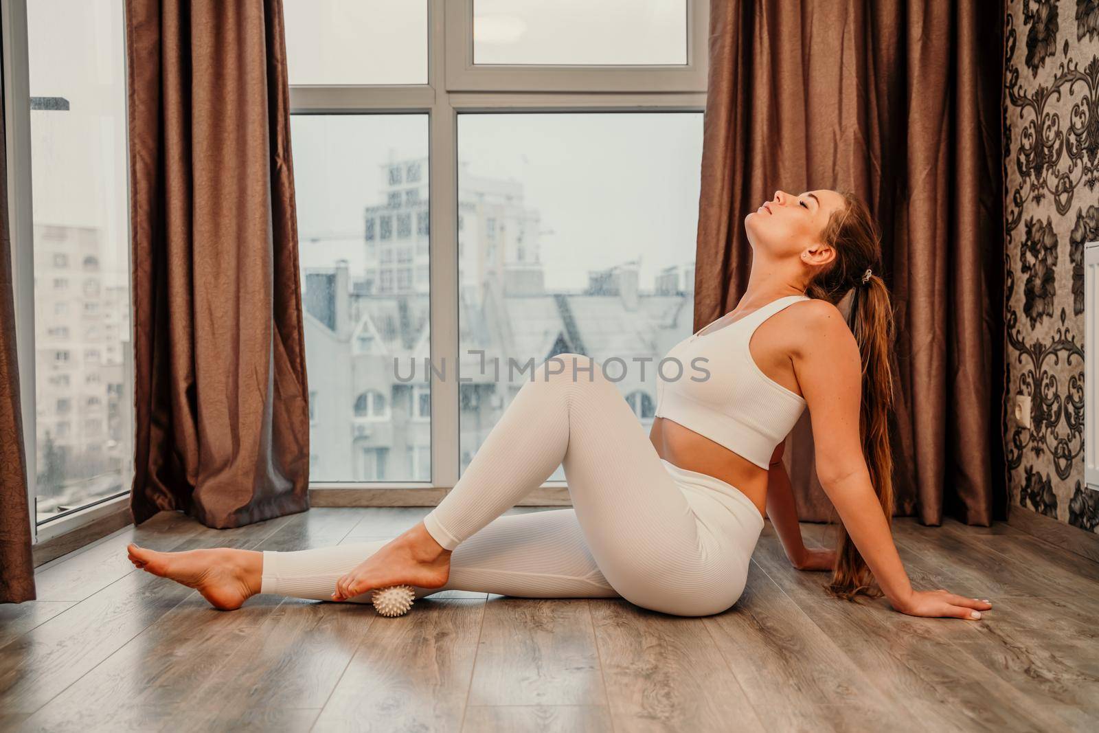 Middle aged athletic attractive woman practicing yoga. Works out at home or in a yoga studio, sportswear, white pants and a full-length top indoors. Healthy lifestyle concept.