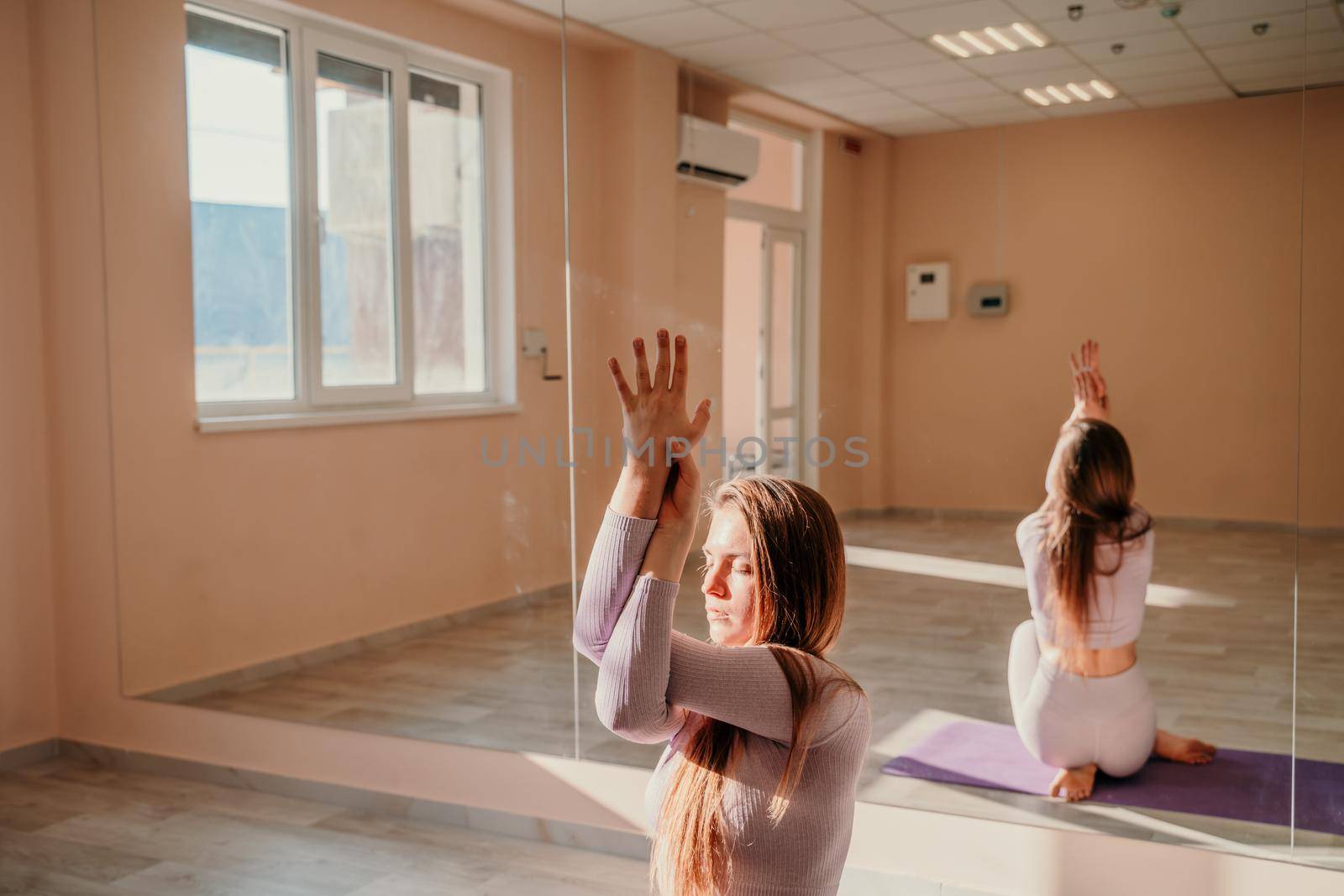 View from above. A beautiful young woman in pink sportswear is engaged in yoga, sports in the hall on a purple rug. Yoga, sport and healthy concept. by Matiunina