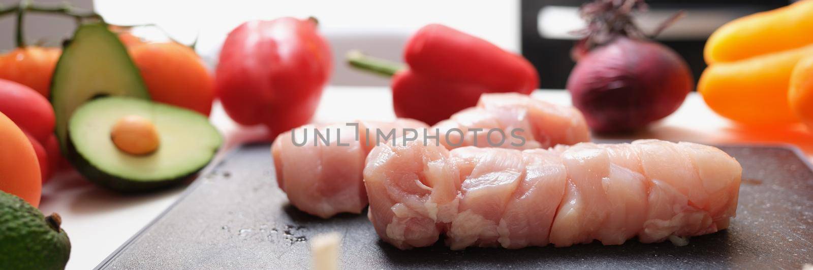 Chicken meat on a cutting board and vegetables on the table, close-up. Cooking at home, organic dish recipe