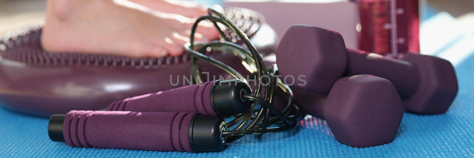 A man at home stands on a massage mat, legs close-up. Sports equipment for exercise, dumbbells and skipping rope