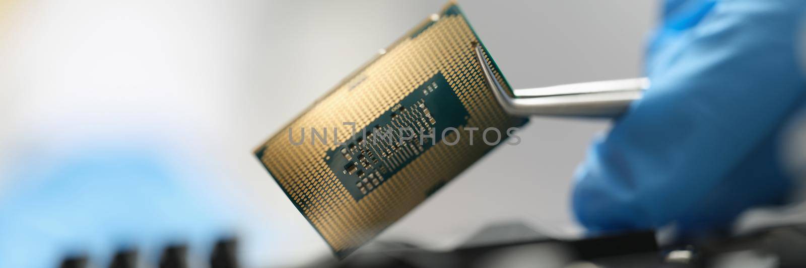 The master is holding a chip over the device with tweezers, close-up, blurry. Microcircuit in the electronics industry