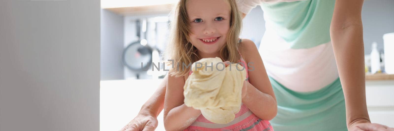 Little girl shows the dough and smiles, close-up. Raising children, mom devotes time to her daughter