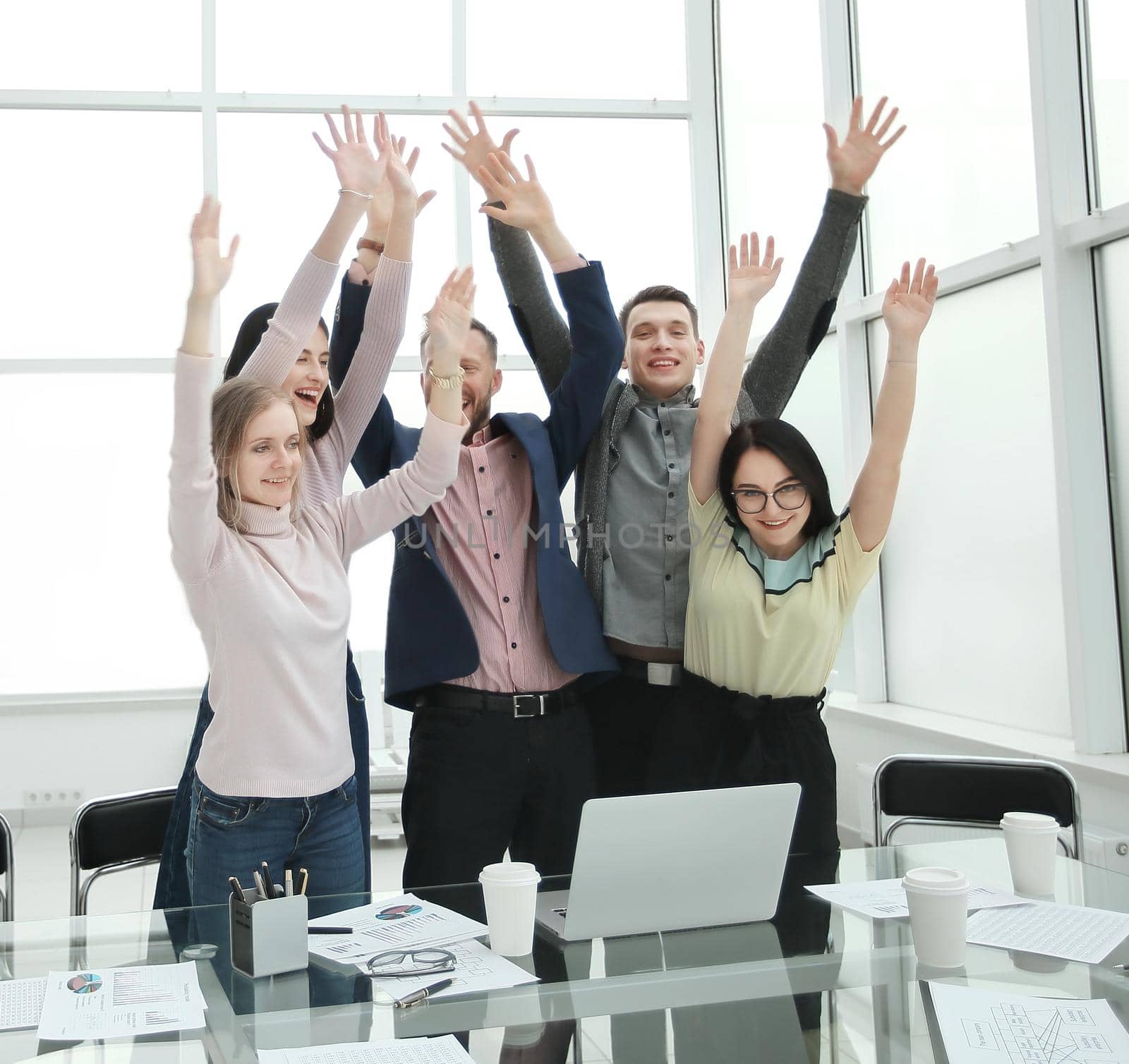 happy business team standing near the desktop with hands up. concept of success
