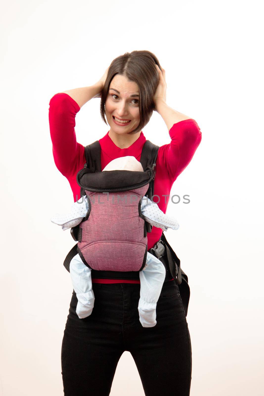 Confused young mother with baby in baby carrier. Isolated on white.