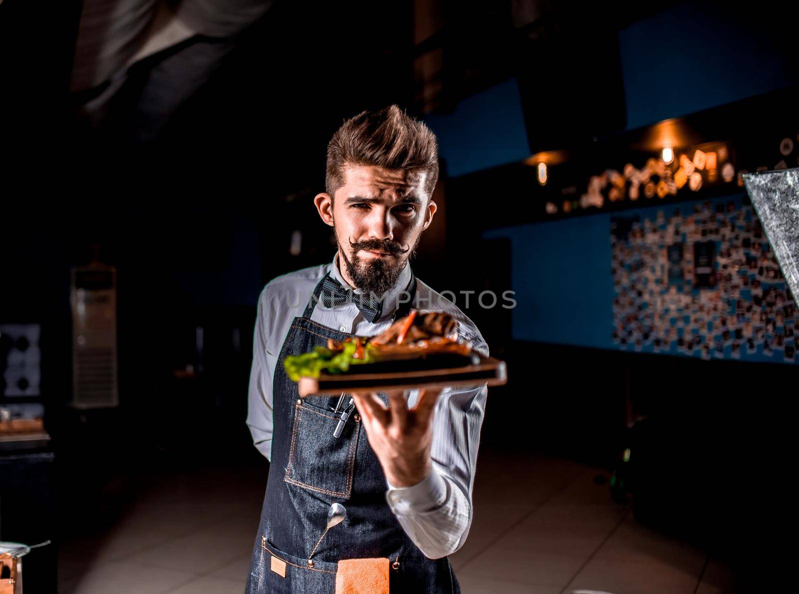 Charismatic waiter helpfully holds salad on a black background.