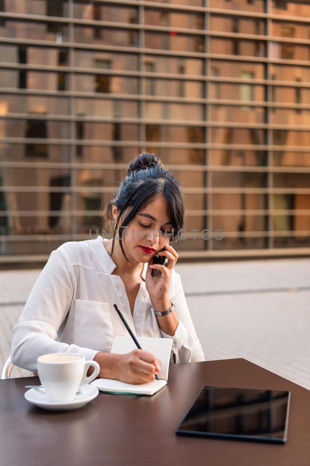 businesswoman working and talking on the phone on the terrace of a coffee shop, concept of digital entrepreneur and urban lifestyle, copy space for text