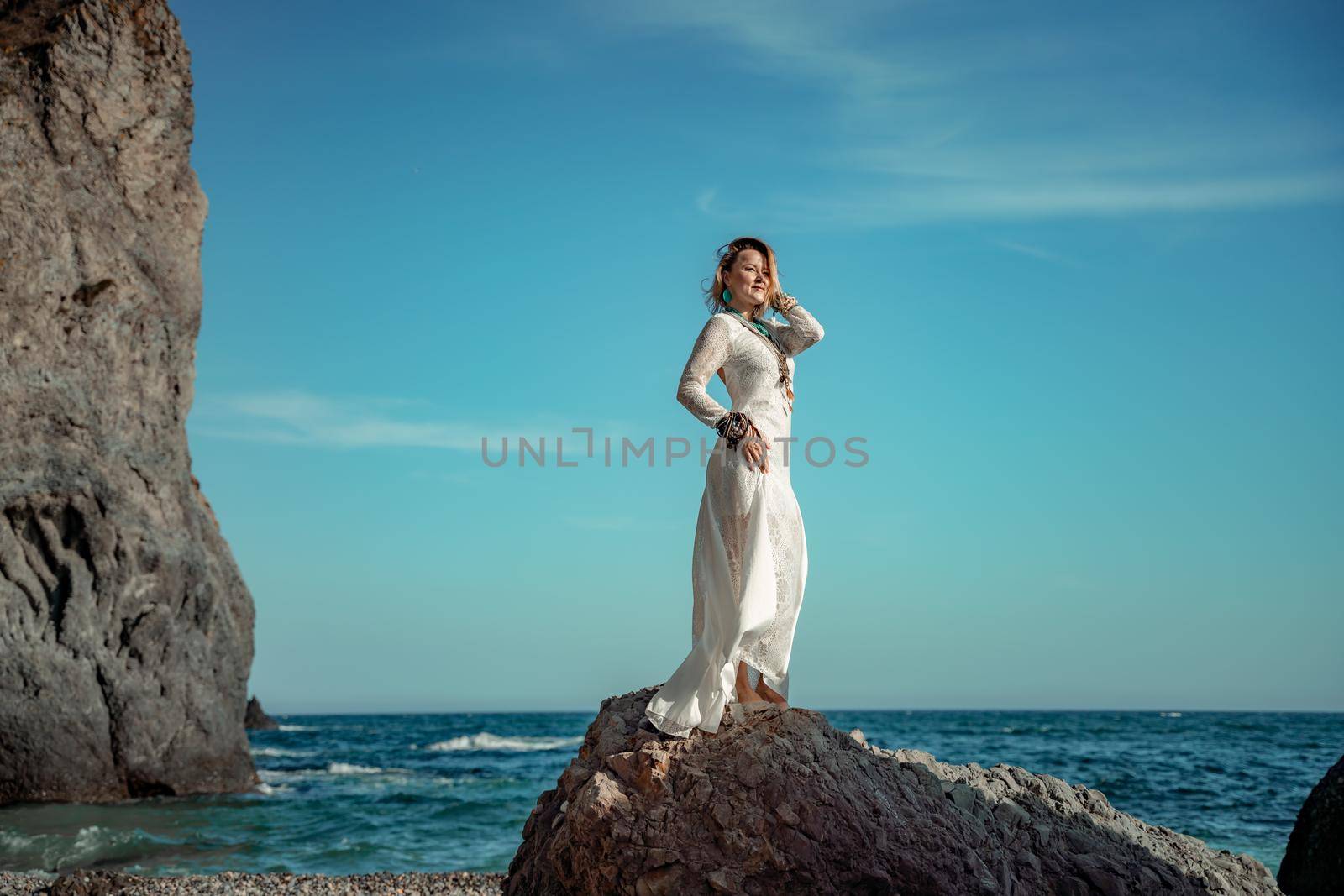 Middle aged woman looks good with blond hair, boho style in white long dress on the beach decorations on her neck and arms