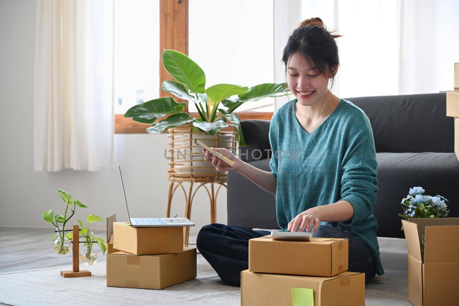 Happy asian woman online seller sitting in modern home office and preparing parcel for delivery. Online selling, E-commerce concept.