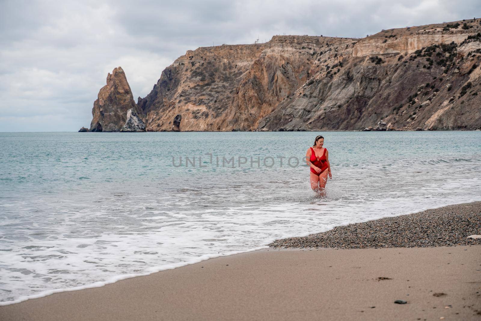 Woman in a bathing suit at the sea. A fat young woman in a red swimsuit enters the water during the surf by Matiunina