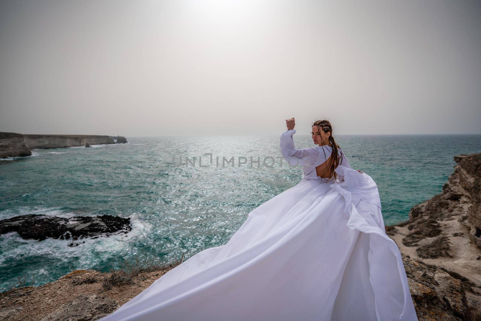 Happy freedom woman on the beach enjoying and posing in white dress. Rear view of a girl in a fluttering white dress in the wind. Holidays, holidays at sea