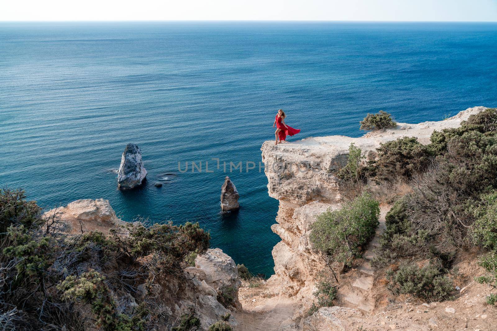 A woman in a red flying dress fluttering in the wind, against the backdrop of the sea. by Matiunina