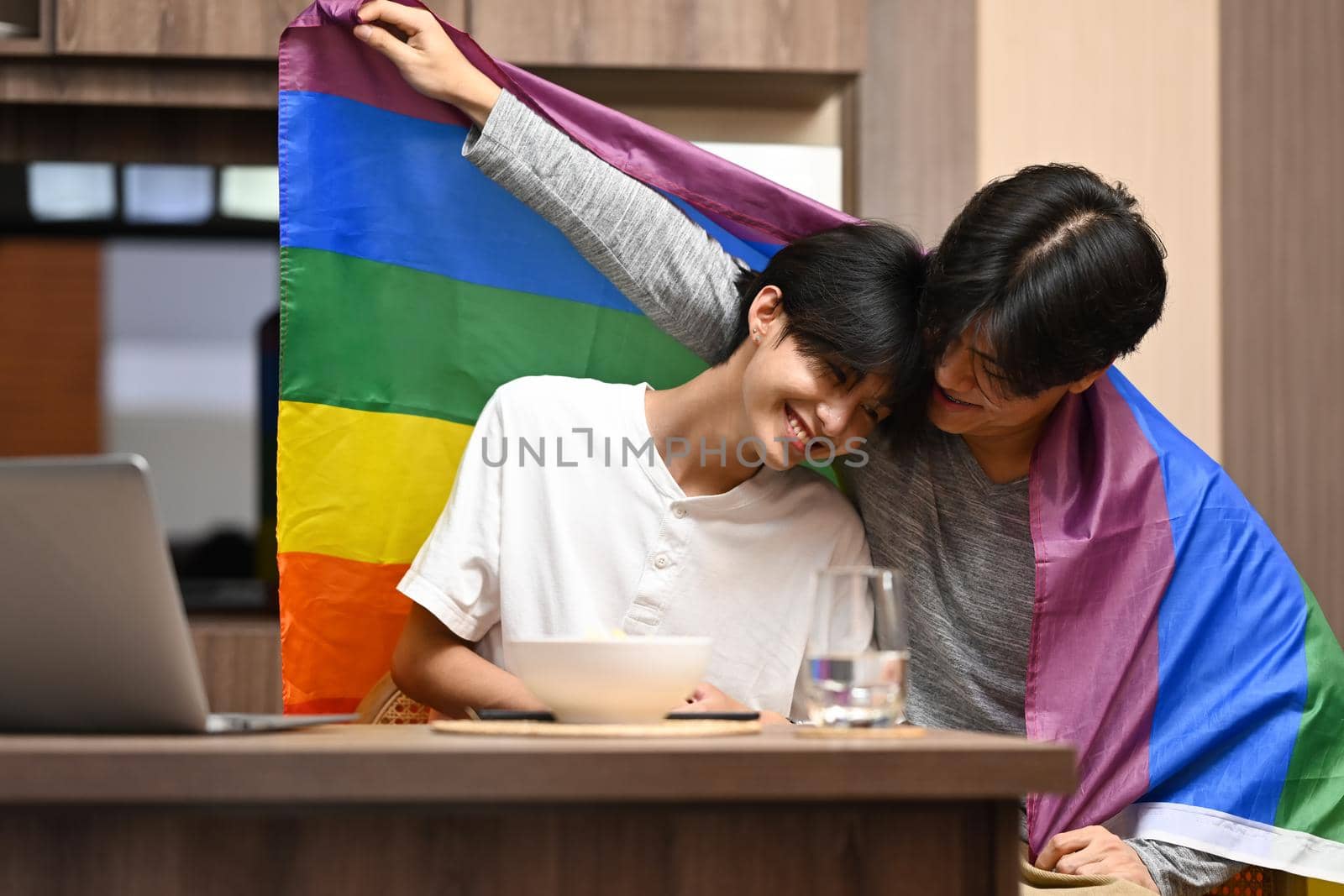 Young gay couple embracing and showing their love with rainbow flag. Concept of sexual freedom and equal rights for LGBT community by prathanchorruangsak