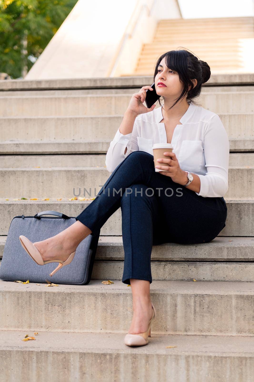 business woman talking on the phone sitting on a concrete staircase with a take away coffee in the other hand, concept of entrepreneur and urban lifestyle