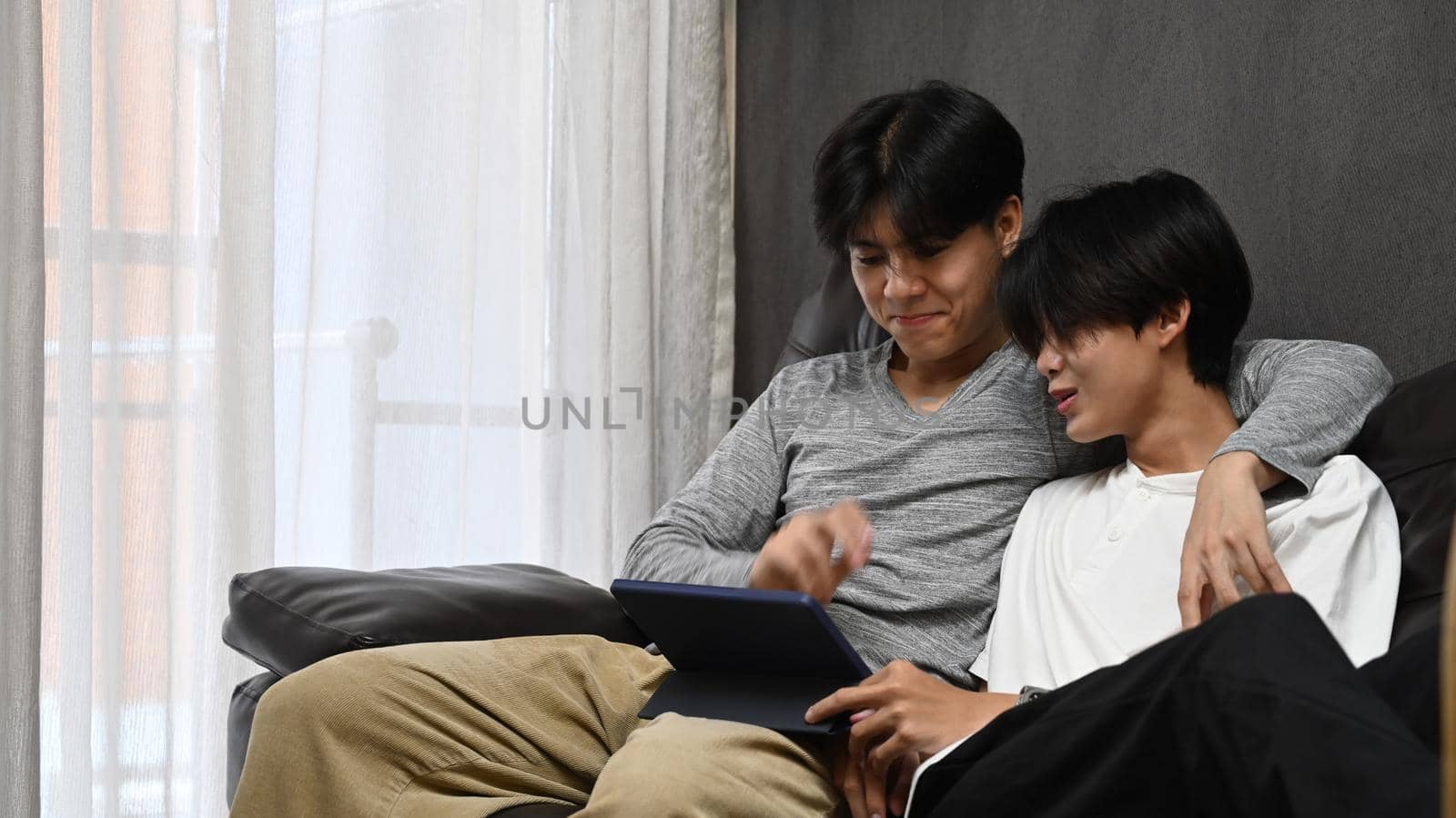 Happy homosexual couple embracing and using digital tablet together on sofa. LGBT and love concept by prathanchorruangsak