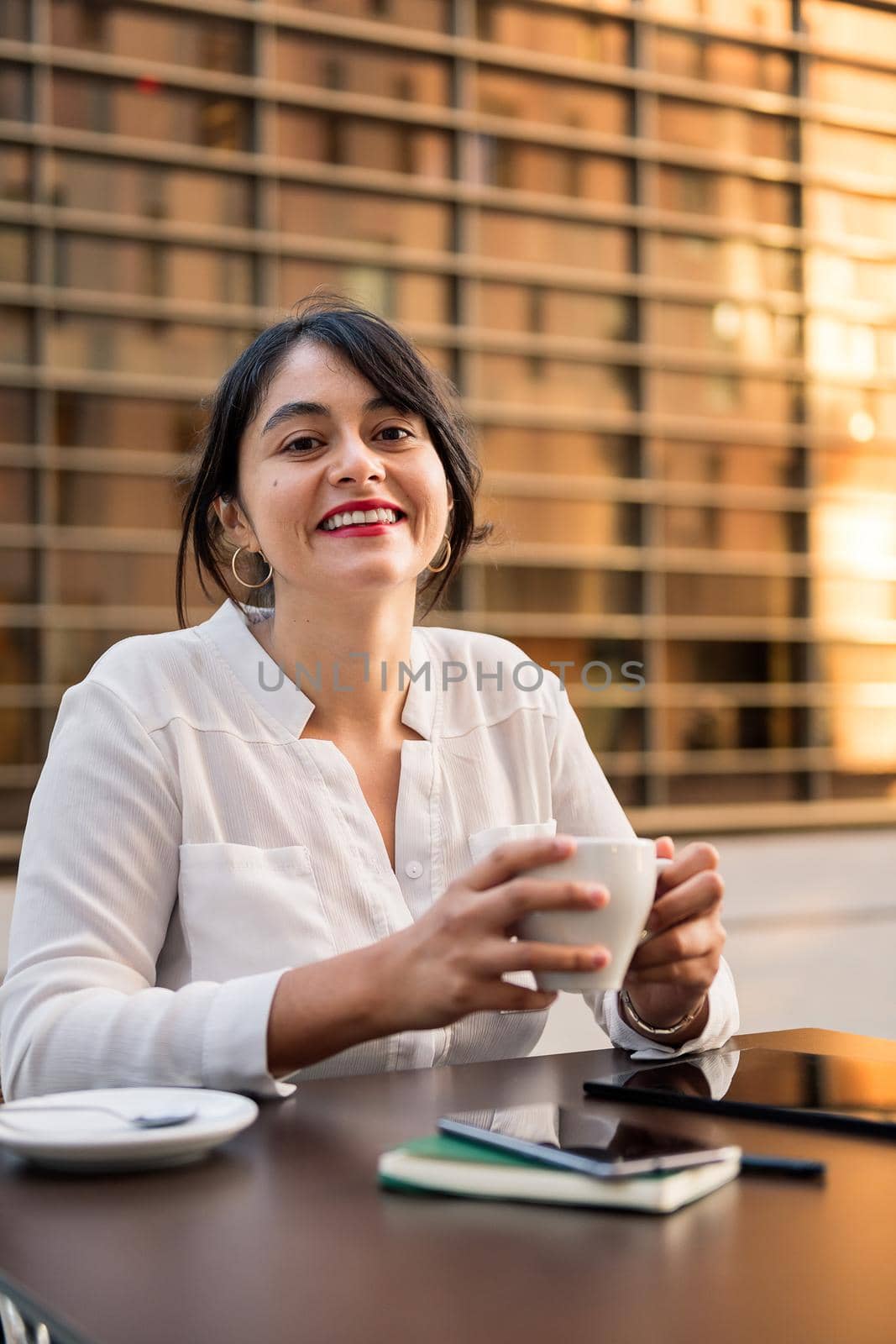 smiling businesswoman working and drinking coffee on the terrace of a coffee shop, concept of digital entrepreneur and urban lifestyle, copy space for text