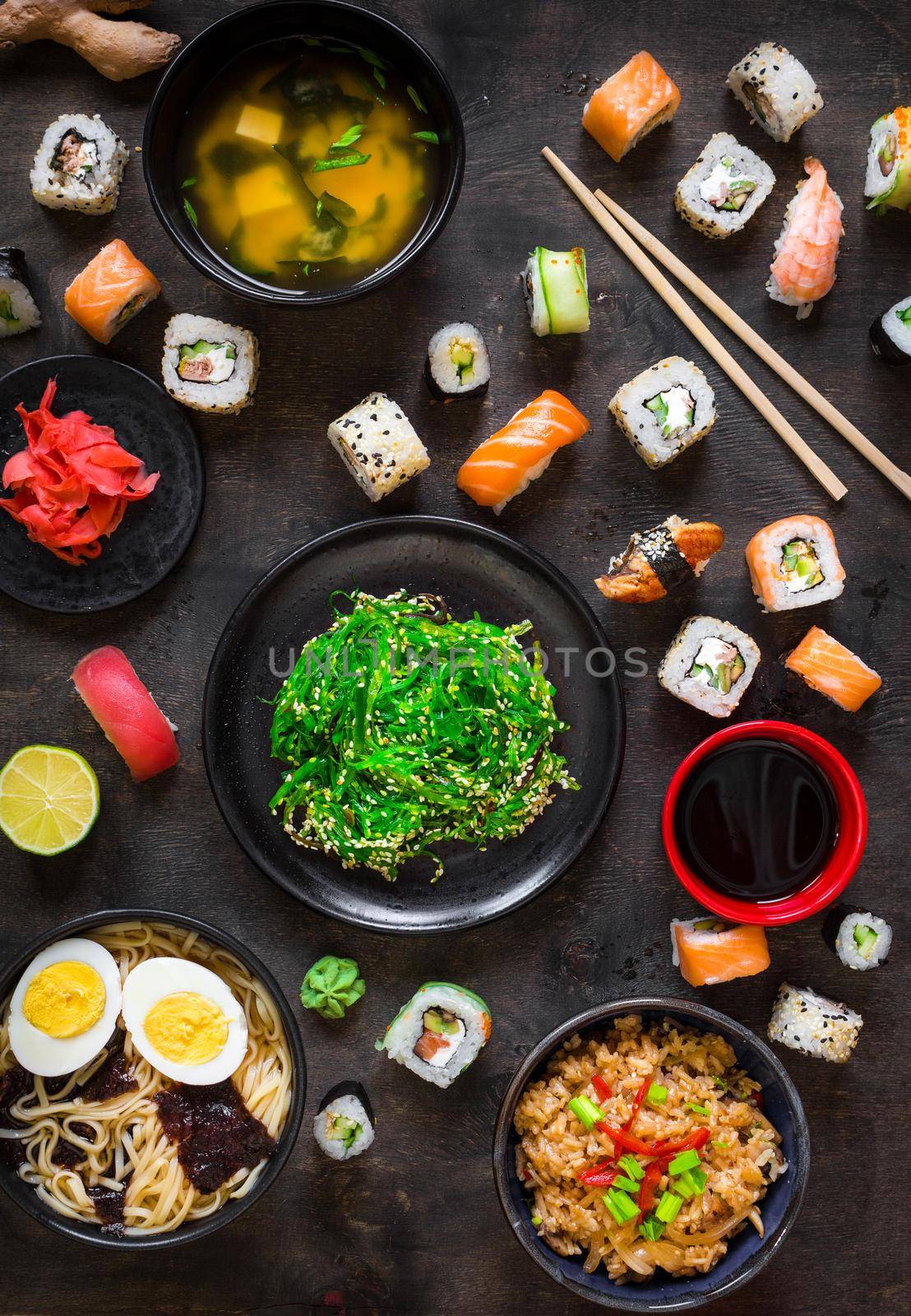 Table served with sushi and traditional japanese food on dark background. Sushi rolls, hiyashi wakame, miso soup, ramen, fried rice with vegetables, nigiri, soy sauce, сhopsticks. Overhead....
