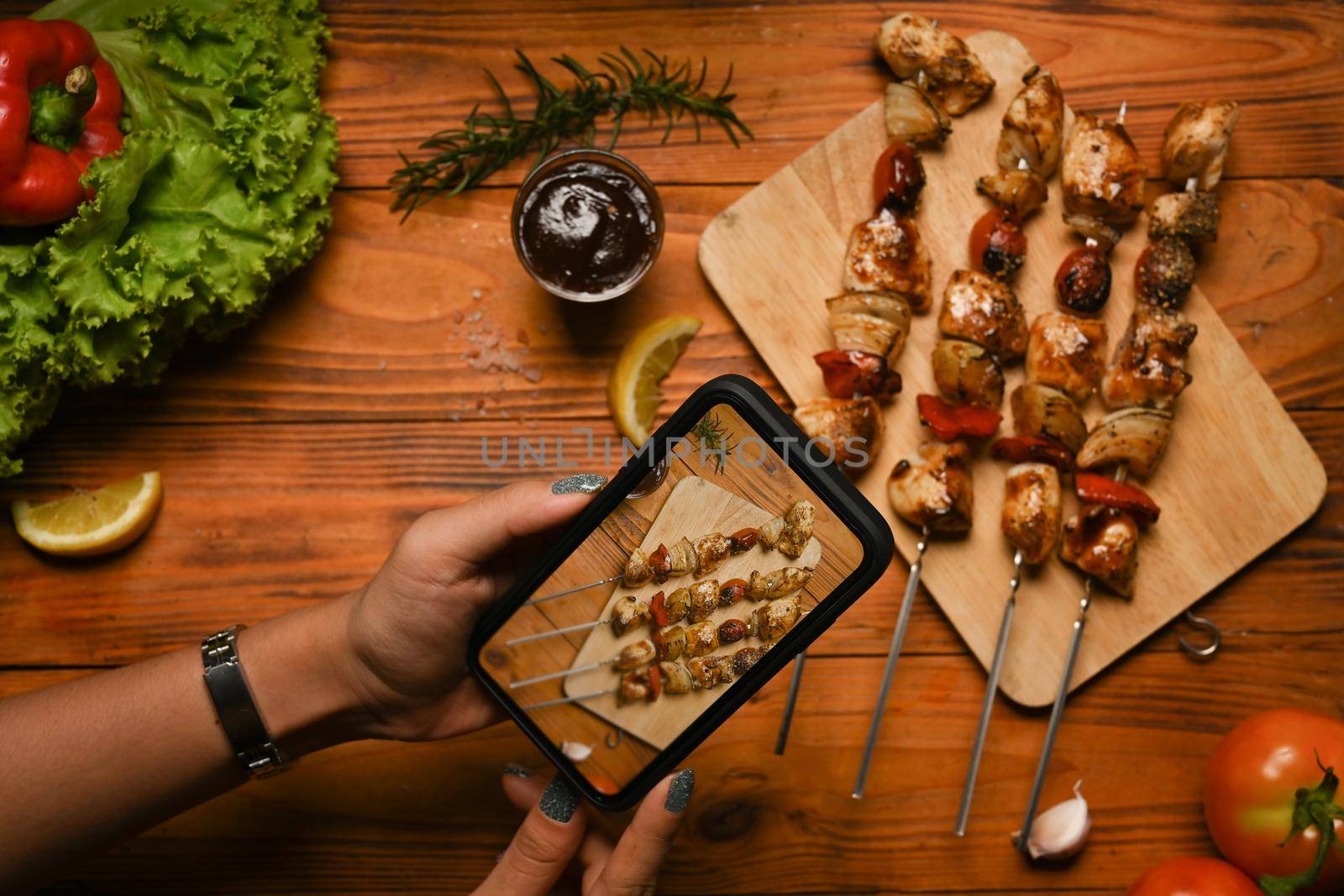 Food blogger using smartphone taking photo of grilled chicken skewers to share on social media by prathanchorruangsak