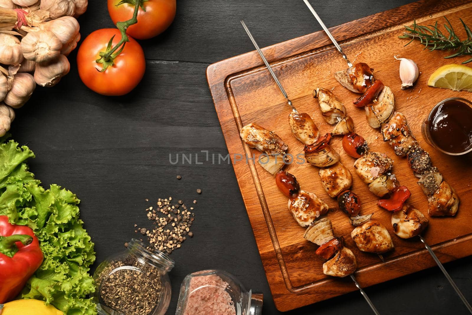 Homemade chicken shish kabobs with tomato, sweet pepper and onions on black wooden table by prathanchorruangsak