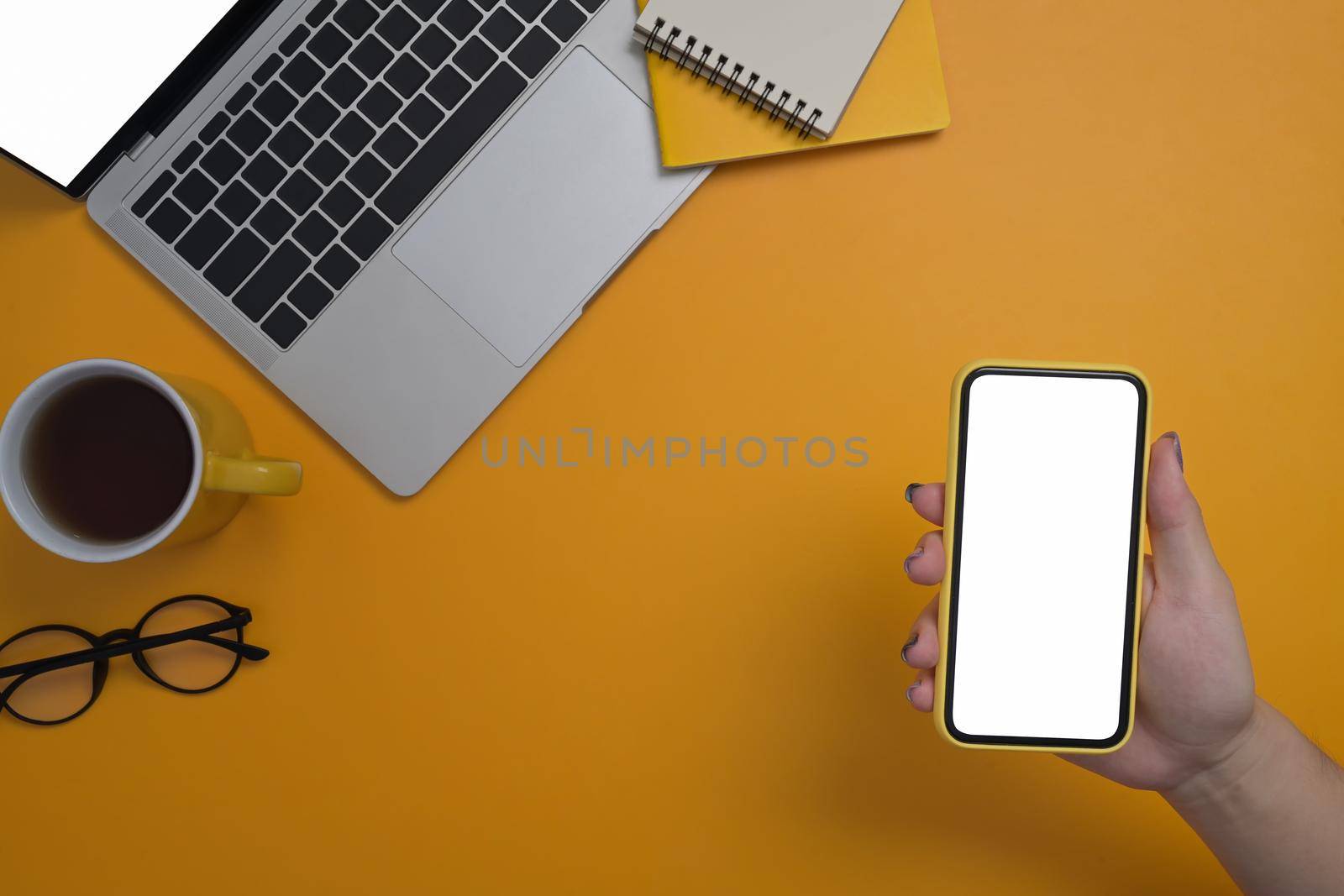 Woman hand holding mockup smart phone with blank screen over yellow background.