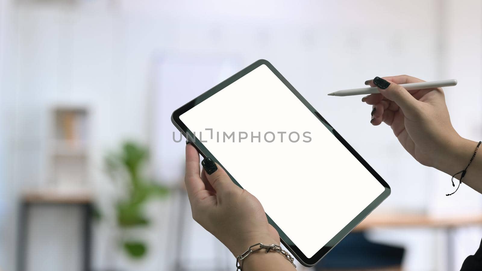 Stylish woman hand holding digital tablet and stylus pen with blurred office background. by prathanchorruangsak