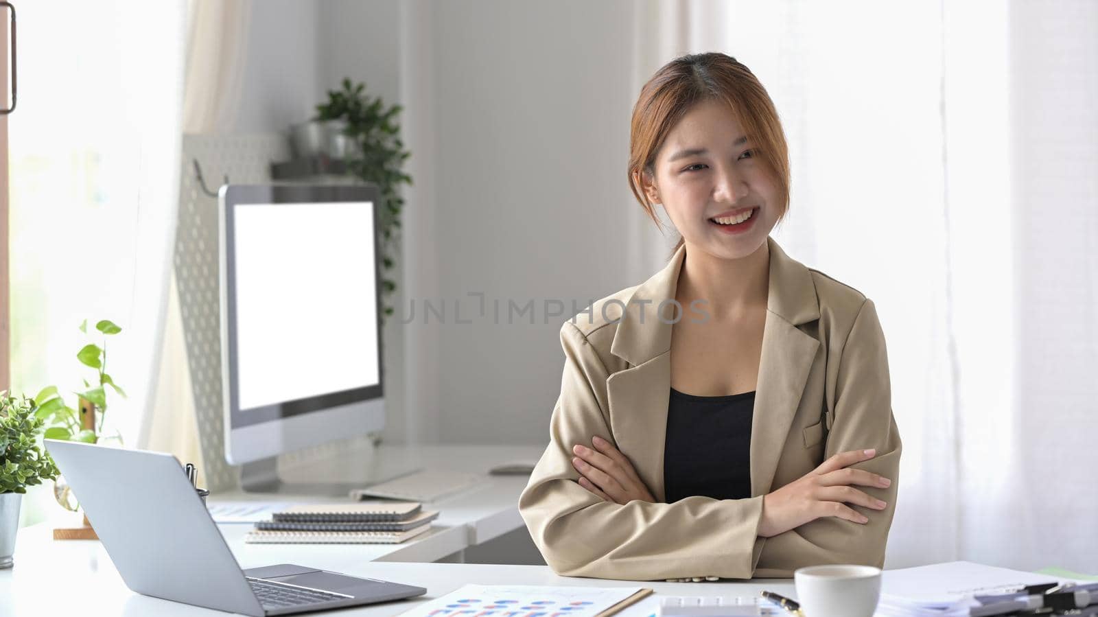 Pretty female employee sitting in modern office and smiling confidently to camera.