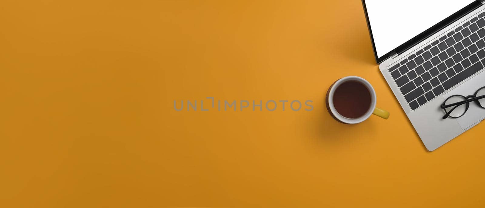 Computer laptop, coffee cup and glasses on yellow background with copy space for your information content.