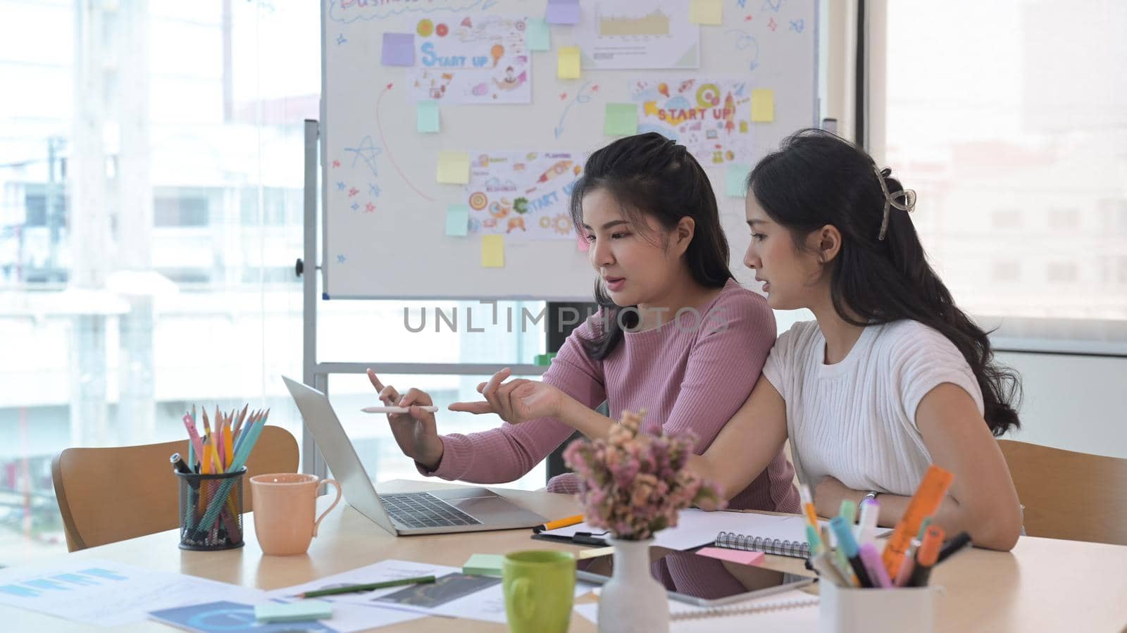 Two creative women looking at laptop screen, discussing new project together.