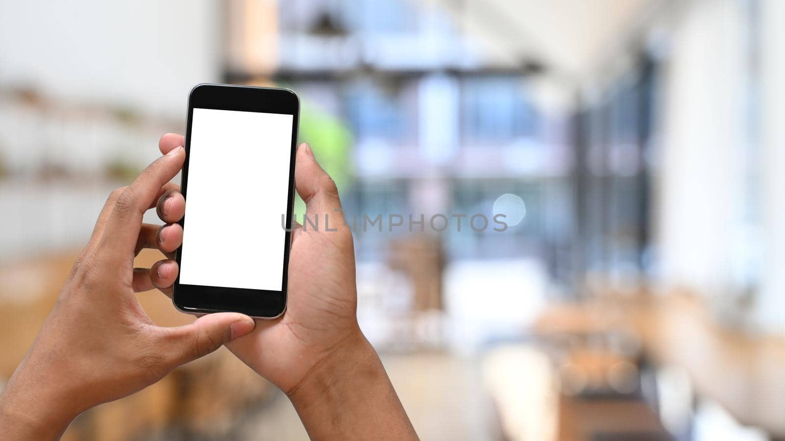 Man hands holding smart phone with blurred cafe background. Empty screen for graphic display montage.