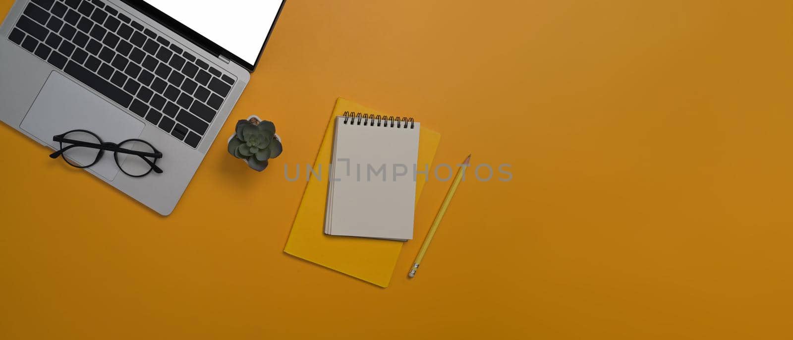 Flat lay laptop computer, notepads and glasses on yellow background with copy space for your information content. by prathanchorruangsak