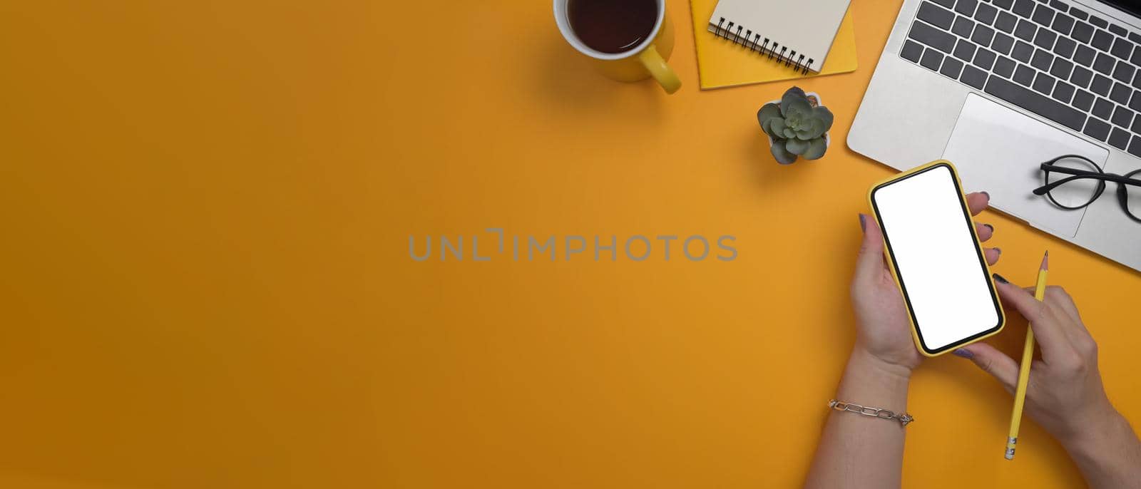 Overhead shot of stylish woman using mobile phone over yellow background. by prathanchorruangsak