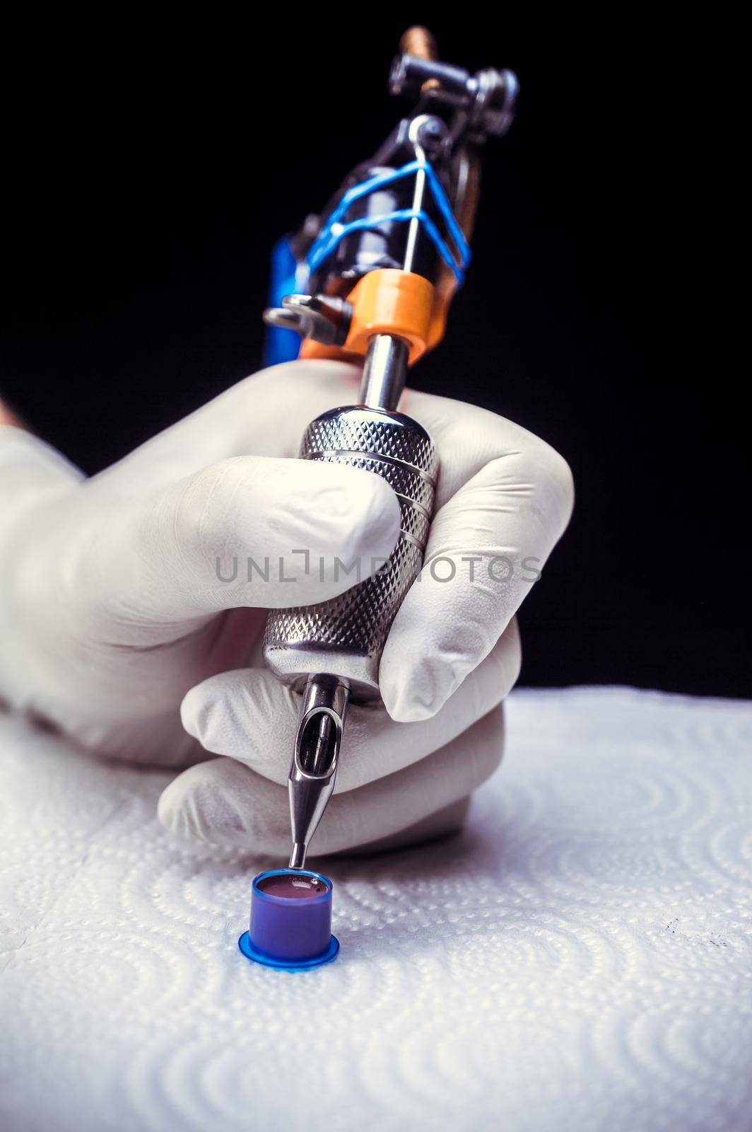 Hand of a tattooer and a tattoo gun./Hand of a tattoo specialist and a tattoo machine.
