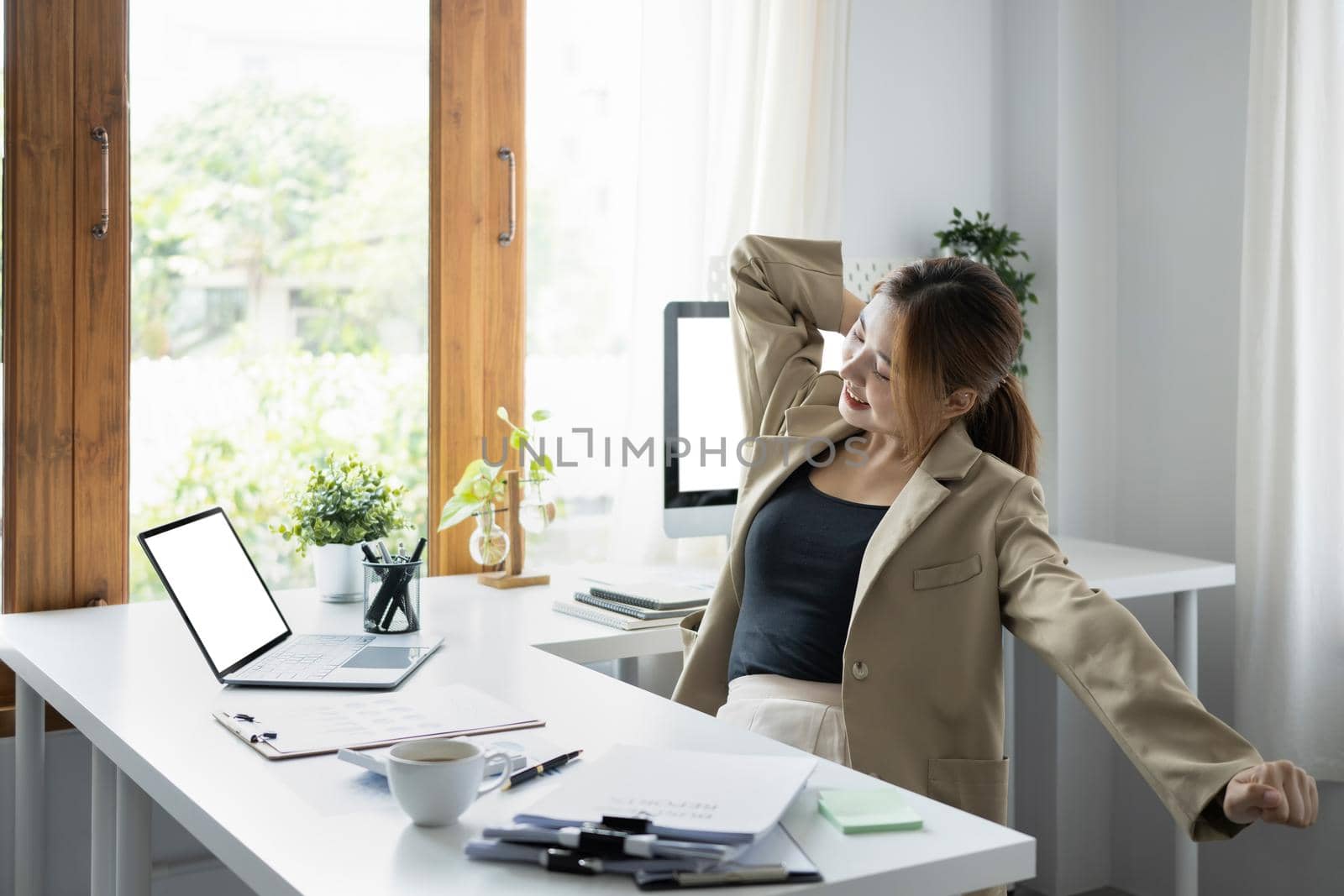 Young female employee stretching arms, relaxing from work in office. by prathanchorruangsak